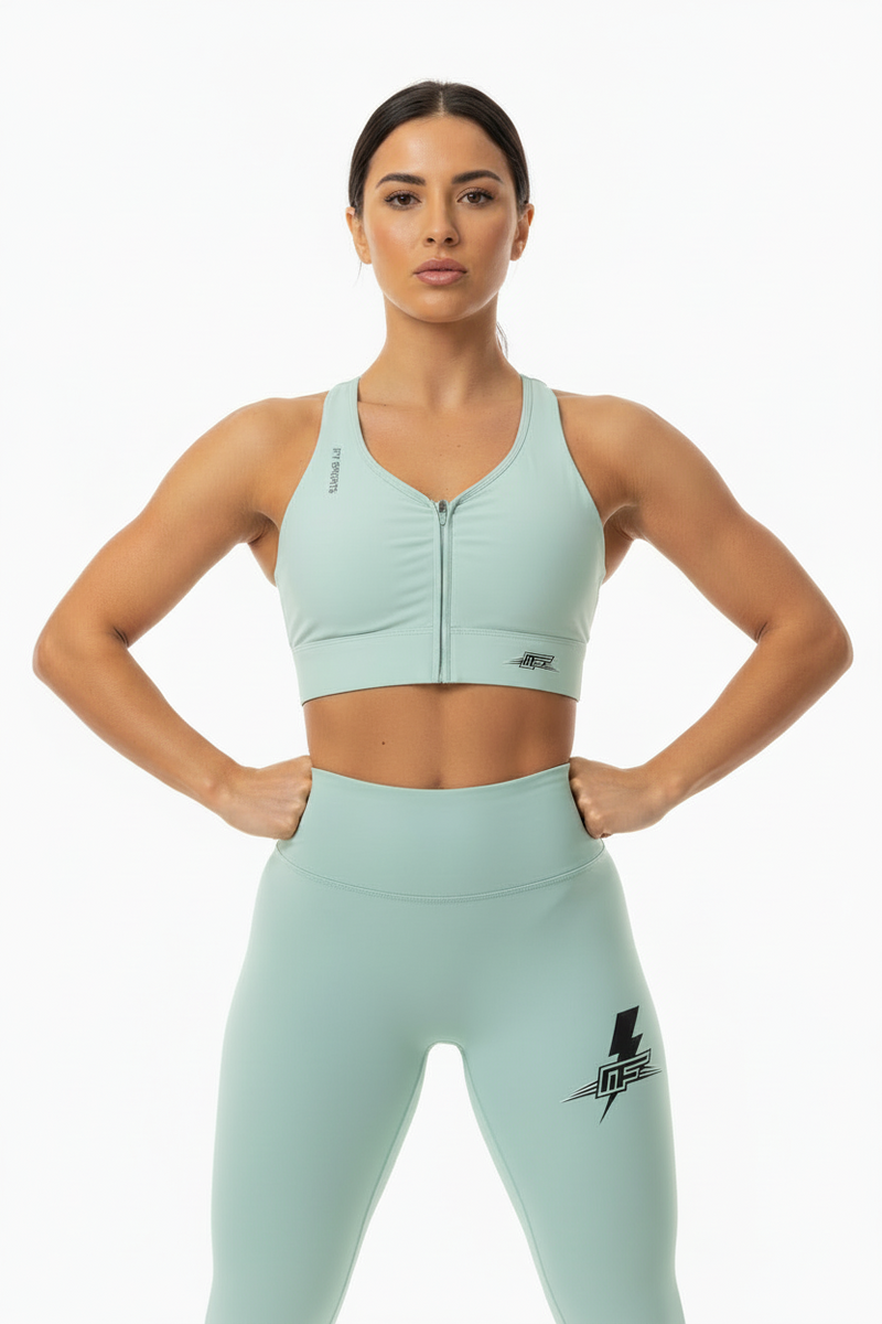 A light mint green athletic sports bra with a front zipper, racerback cut, and ruched detailing, shown on a plain white background. The brand 'LIFT SPORTS' is printed vertically on the left shoulder strap, and a stylized 'LF' logo is on the lower right front.