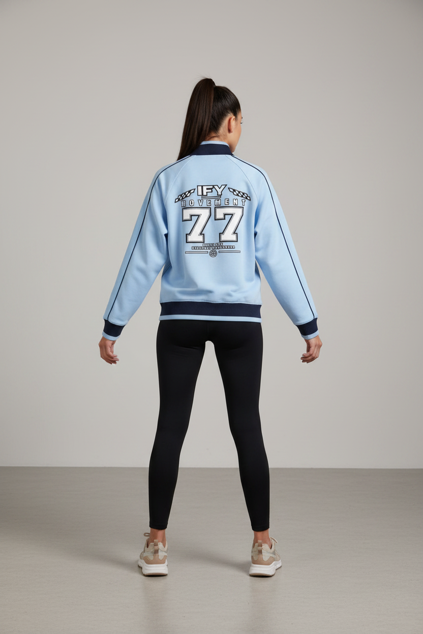A light blue long-sleeve track jacket shown from the back, featuring a dark navy collar, hem, and cuffs, with white and black graphic text reading 'IFY MOVEMENT 77' on the back.