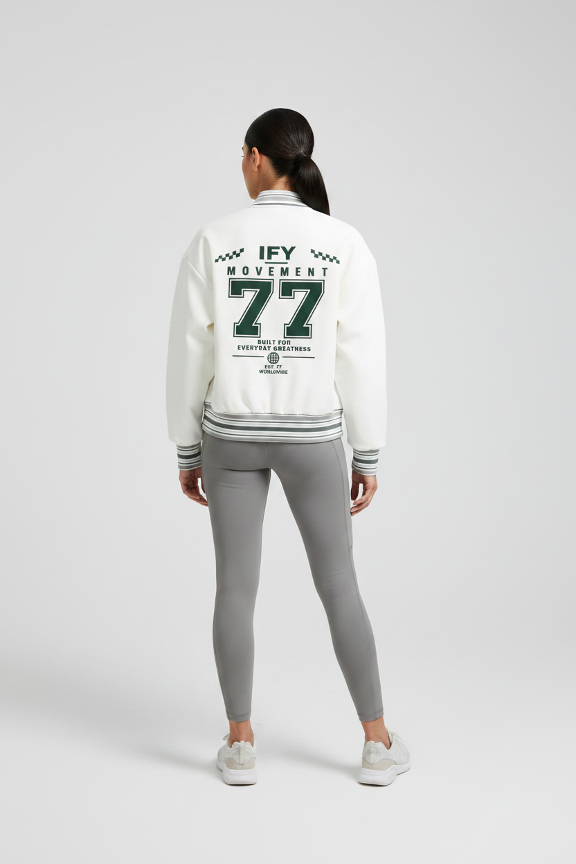 The back of an off-white varsity-style jacket with dark green and gray striped ribbed collar, cuffs, and hem. The back features a large graphic print reading 'IFY MOVEMENT 77' in dark green and gray.