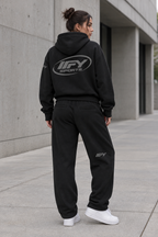 Female model showing the back of the black IFY hoodie and sweatpants set with white Air Force 1 trainers
