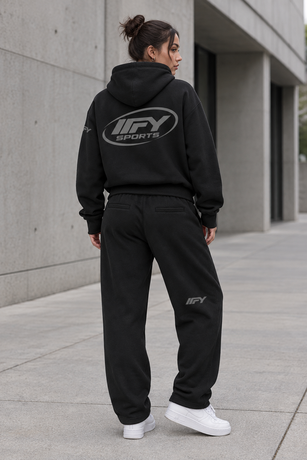 Female model showing the back of the black IFY hoodie and sweatpants set with white Air Force 1 trainers