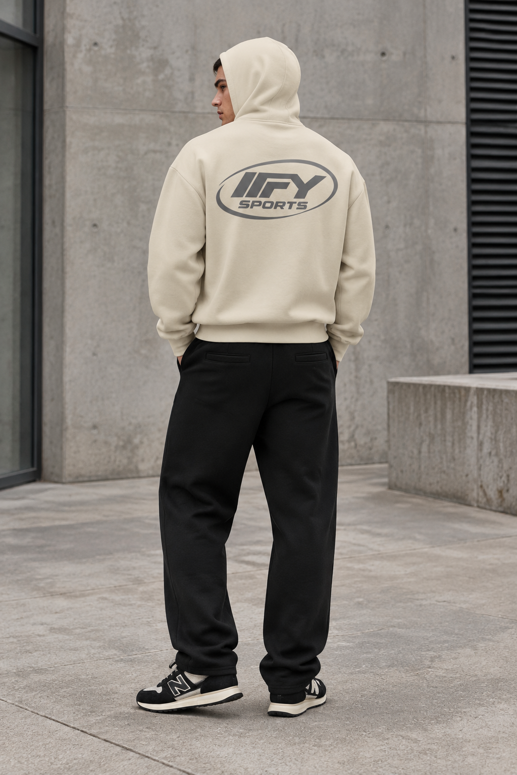 Male model wearing the cream IFY hoodie and black sweatpants from the back, hood up, with New Balance 370 trainers